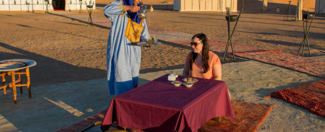 Berber host serving traditional Moroccan tea to traveler at luxury private desert camp in Merzouga Sahara Morocco