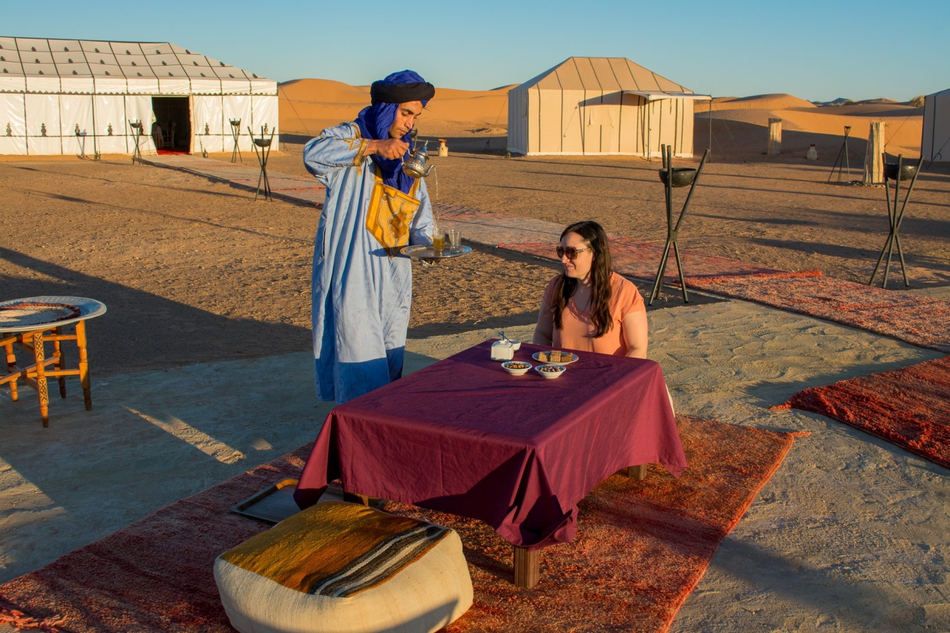 Berber host serving traditional Moroccan tea to traveler at luxury private desert camp in Merzouga Sahara Morocco